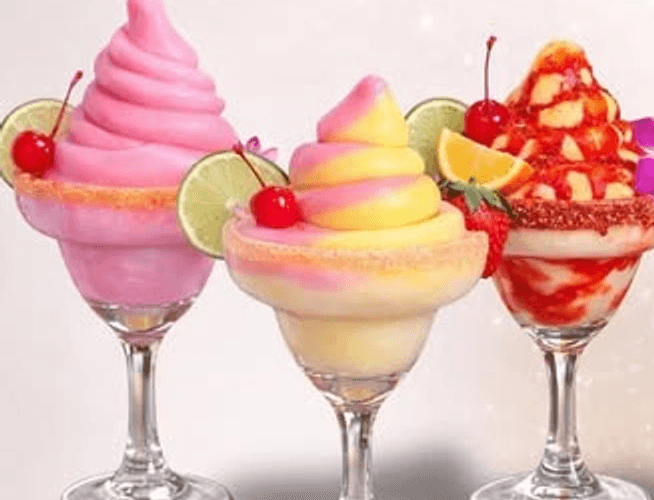 Three soft serve margaritas in salt-rimmed glasses, garnished with lime, cherry and fruit